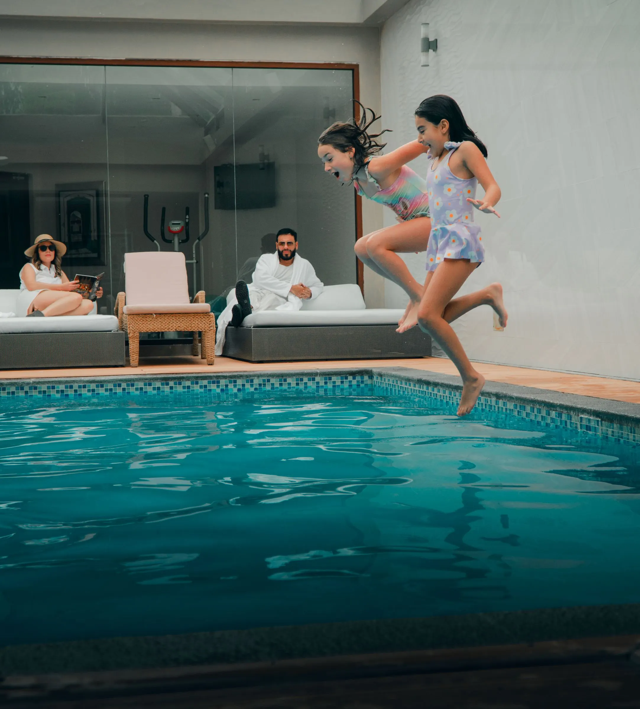 Niños saltando a la piscina cubierta mientras la familia mira