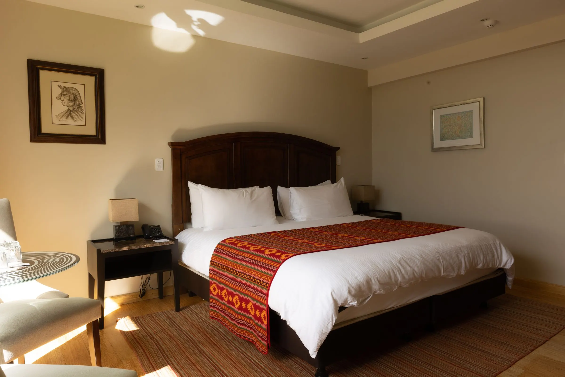 Habitación King Estándar con cama tendida en blanco y manta andina a los pies